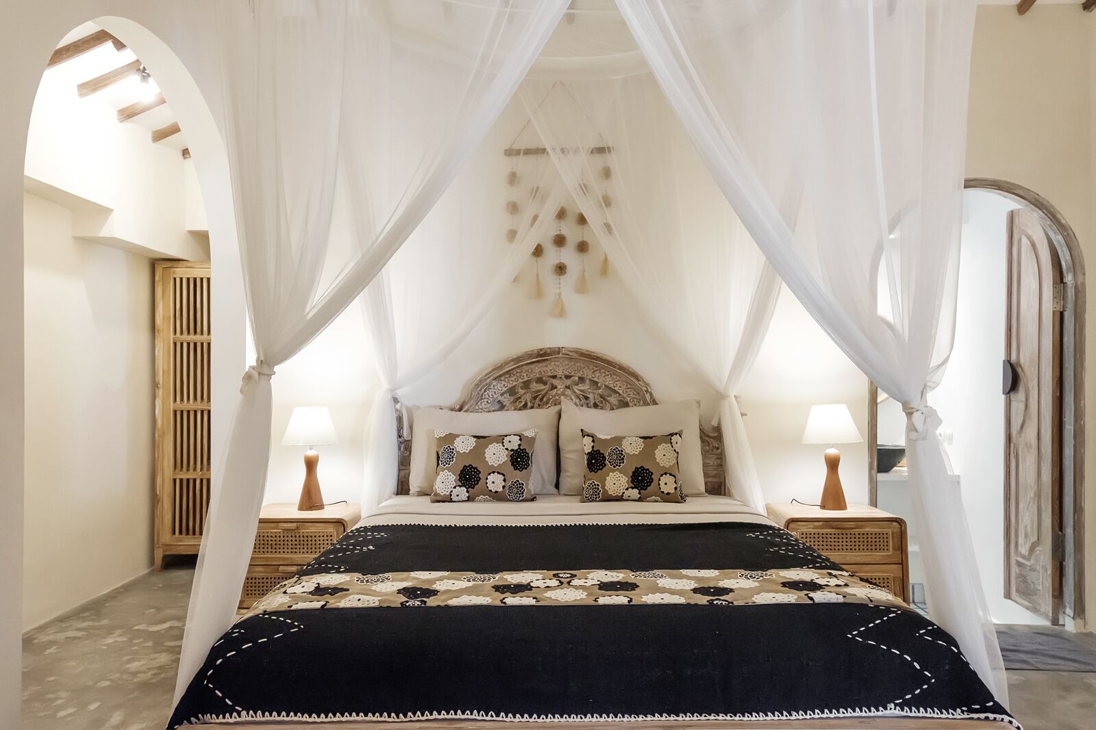 A bedroom with a four-poster canopy bed, two bedside tables with lamps, and a decorative wall hanging above the bed.