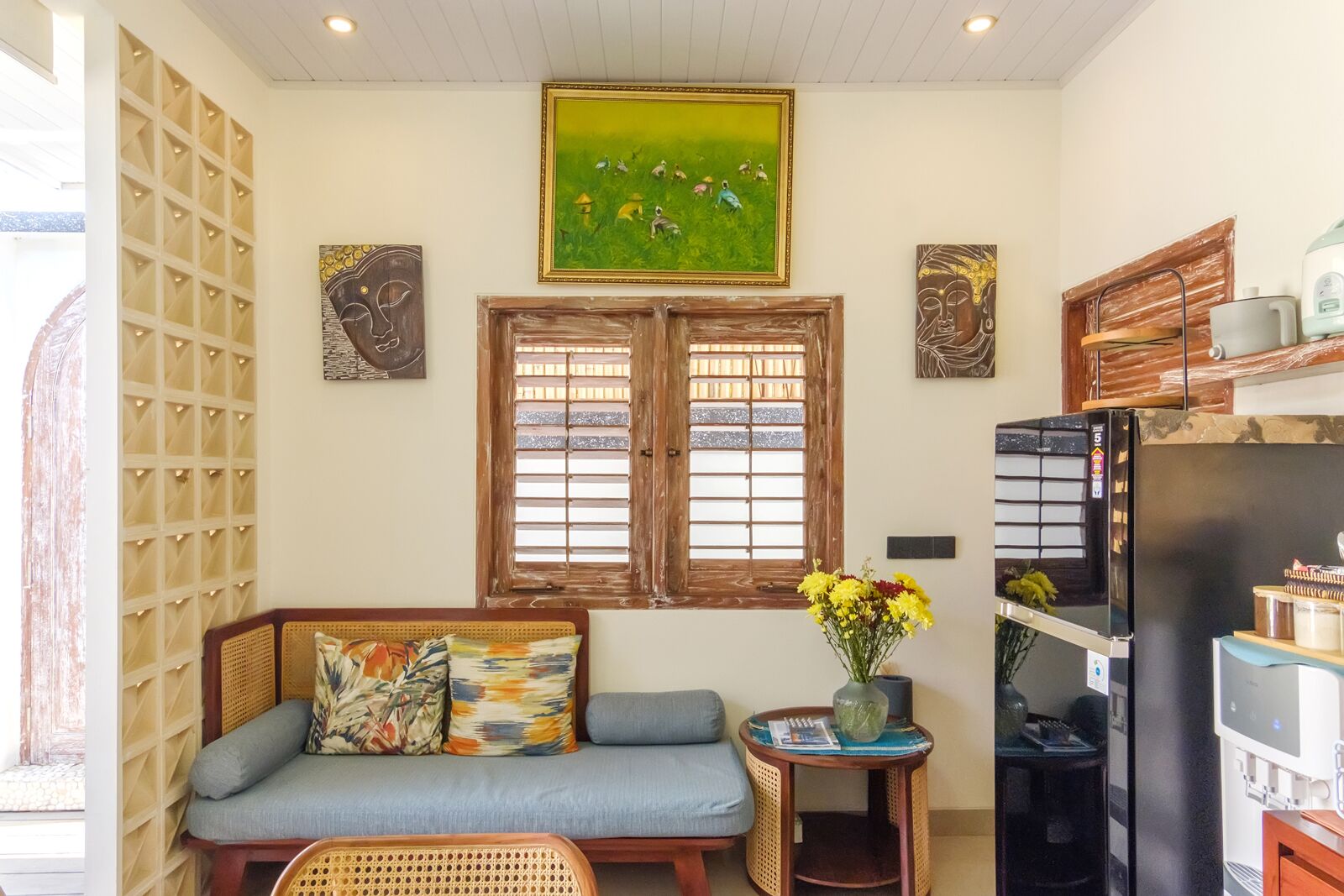 A living room with a sofa, a small table with a vase of flowers, a refrigerator, and artwork on the walls.