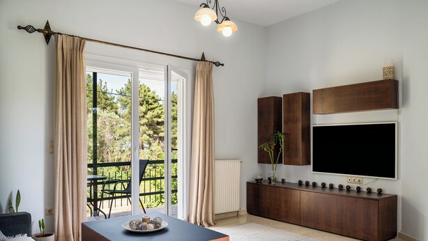 A modern living room with a large TV, wooden furniture, a dining table, and a view of the outdoors. - The Olive Grove Two-Bedroom Apartment by Konnect, Dassia  (Corfu)