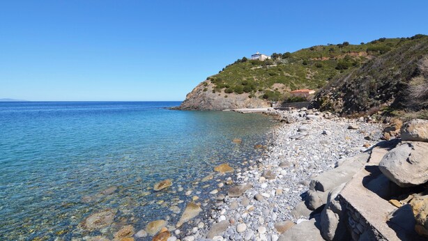 A coastal landscape with a rocky beach, clear blue sea, and a hill with buildings. - Casa Gelso, Vista Mare e Relax Nella Natura (Patresi)