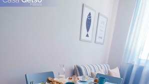A dining area with a white table and blue chairs, a bowl of pears, a plate of pastries, and a blue placemat. - Casa Gelso, Vista Mare e Relax Nella Natura (Patresi)