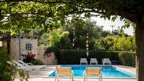 Une piscine avec des chaises longues, un bâtiment en pierre et de la verdure.