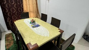 A dining area with a table set for four, a patterned rug, and curtains. - FWA guest house  (Marang)