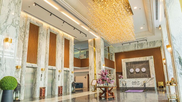 Un hall con columnas de mármol, ascensores, una recepción y un elemento decorativo en el techo.