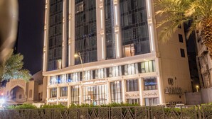 Un edificio alto y moderno con ventanas amplias y fachada simétrica, rodeado por una valla decorativa y palmeras.