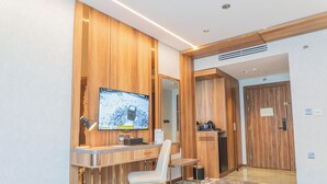 Una habitación moderna con un escritorio de madera, una silla, un televisor de pantalla plana, un espejo y un armario.