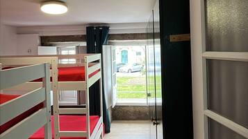 A corridor with bunk beds, a door, and a view of a car outside.