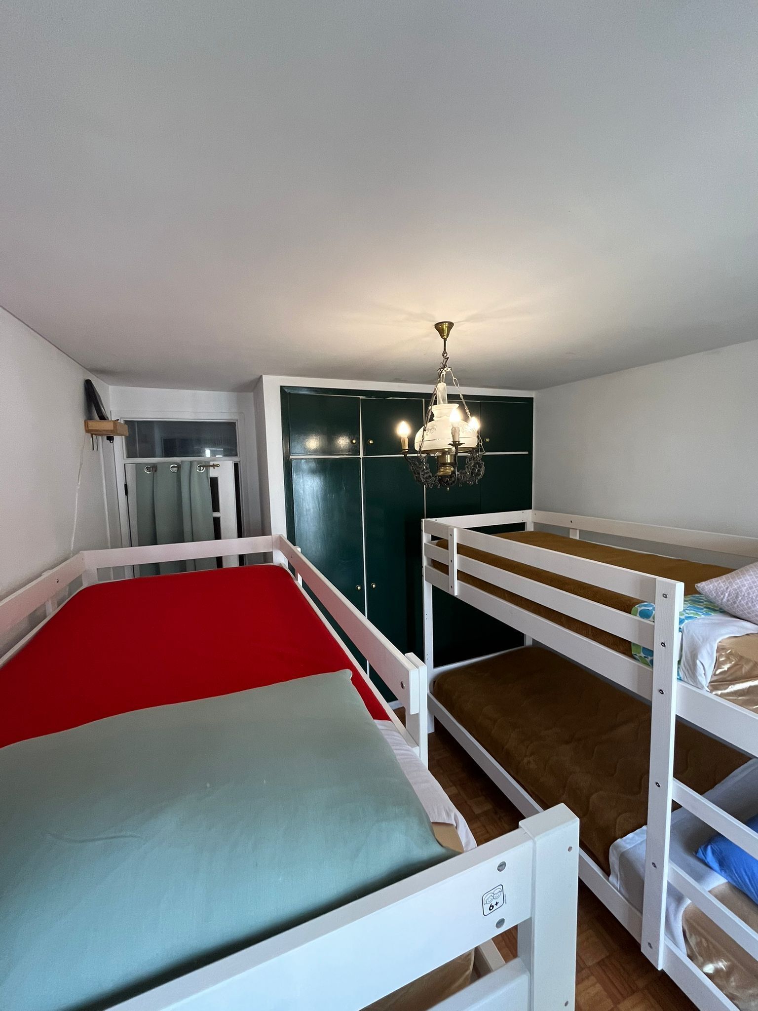 A room with bunk beds, a chandelier, and a green wardrobe.