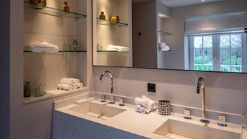 Ein modernes Badezimmer mit einem Doppelwaschbecken, Glastablagen und einem großen Spiegel.