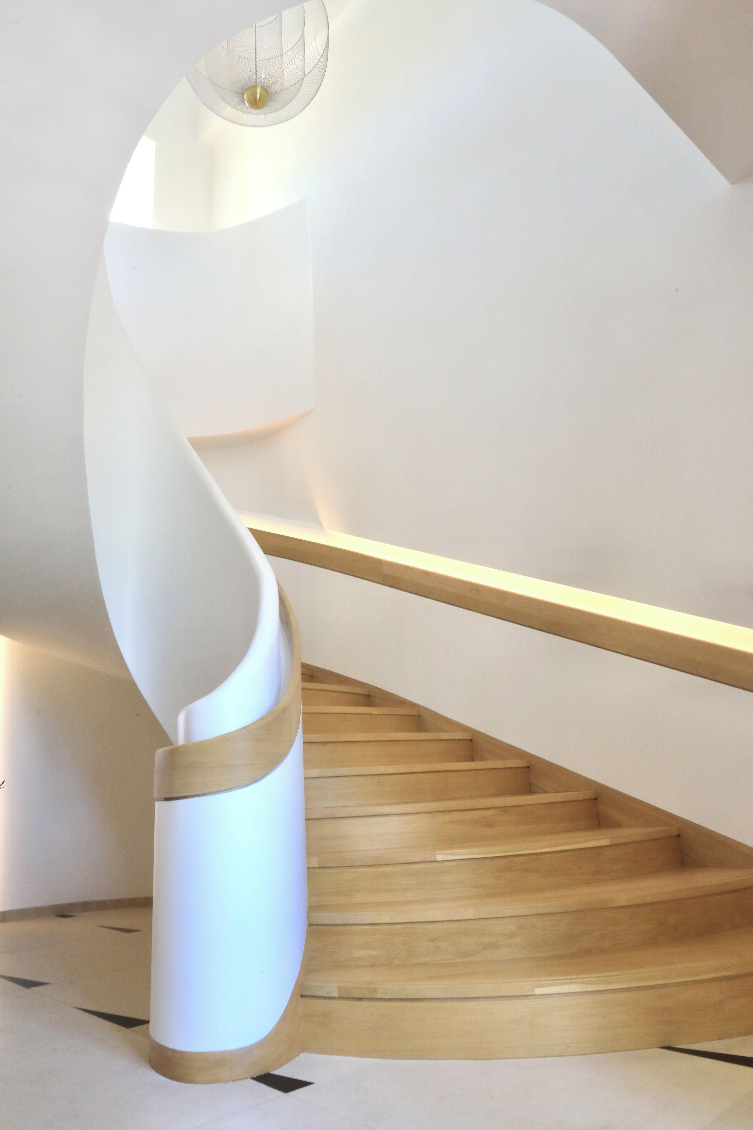 A spiral staircase with a wooden finish and a white handrail.