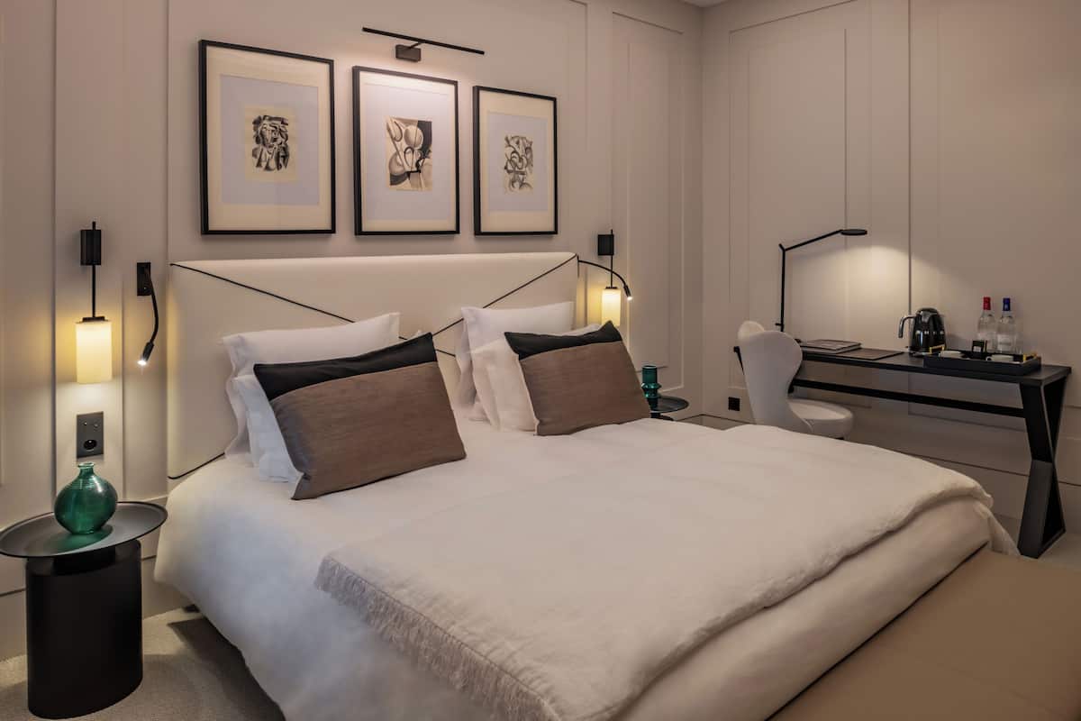 Habitación de hotel moderna con una cama grande, mesitas de noche, un escritorio y cuadros en la pared.
