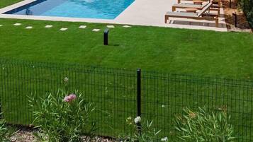 A modern house with a swimming pool, outdoor seating, and a well-maintained lawn.