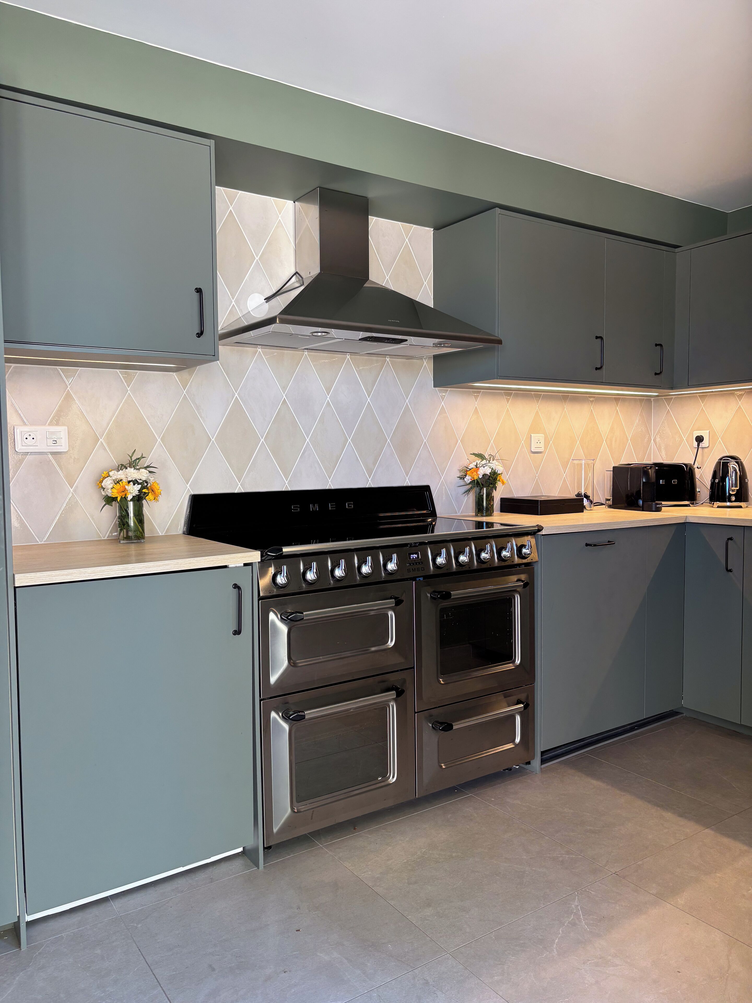 A modern kitchen with grey cabinets, a stainless steel stove, and a tiled backsplash.
