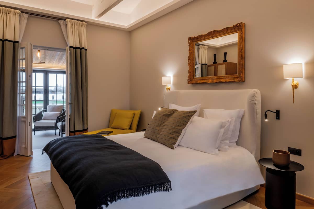 Un dormitorio ordenado con una cama grande, una silla, una mesita y un espejo en la pared.