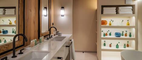 A modern bathroom with a large mirror, two sinks, a bathtub, and shelves with toiletries.
