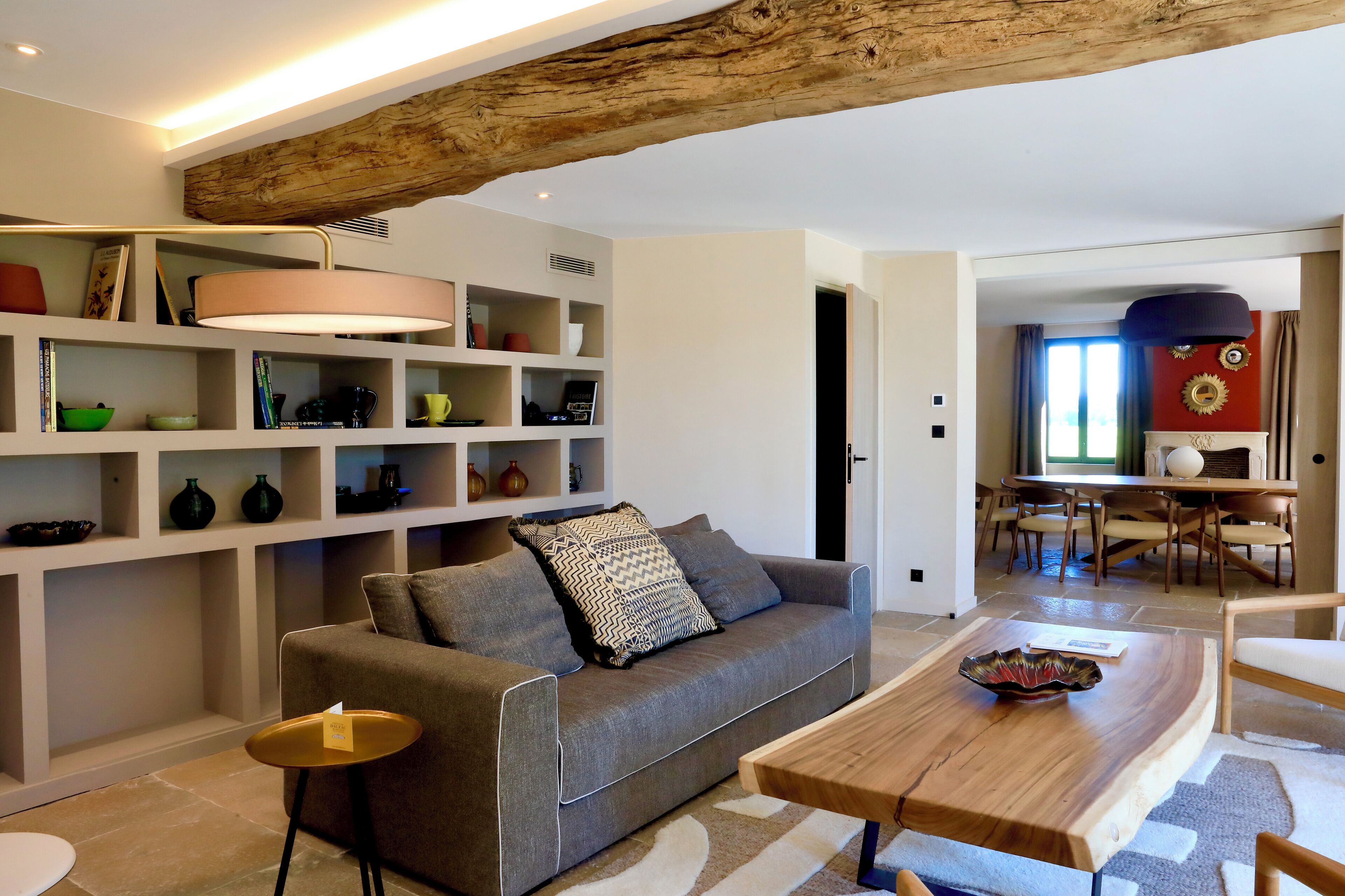 Una sala de estar moderna con un sofá gris, una mesa de centro de madera y una estantería llena de objetos decorativos.