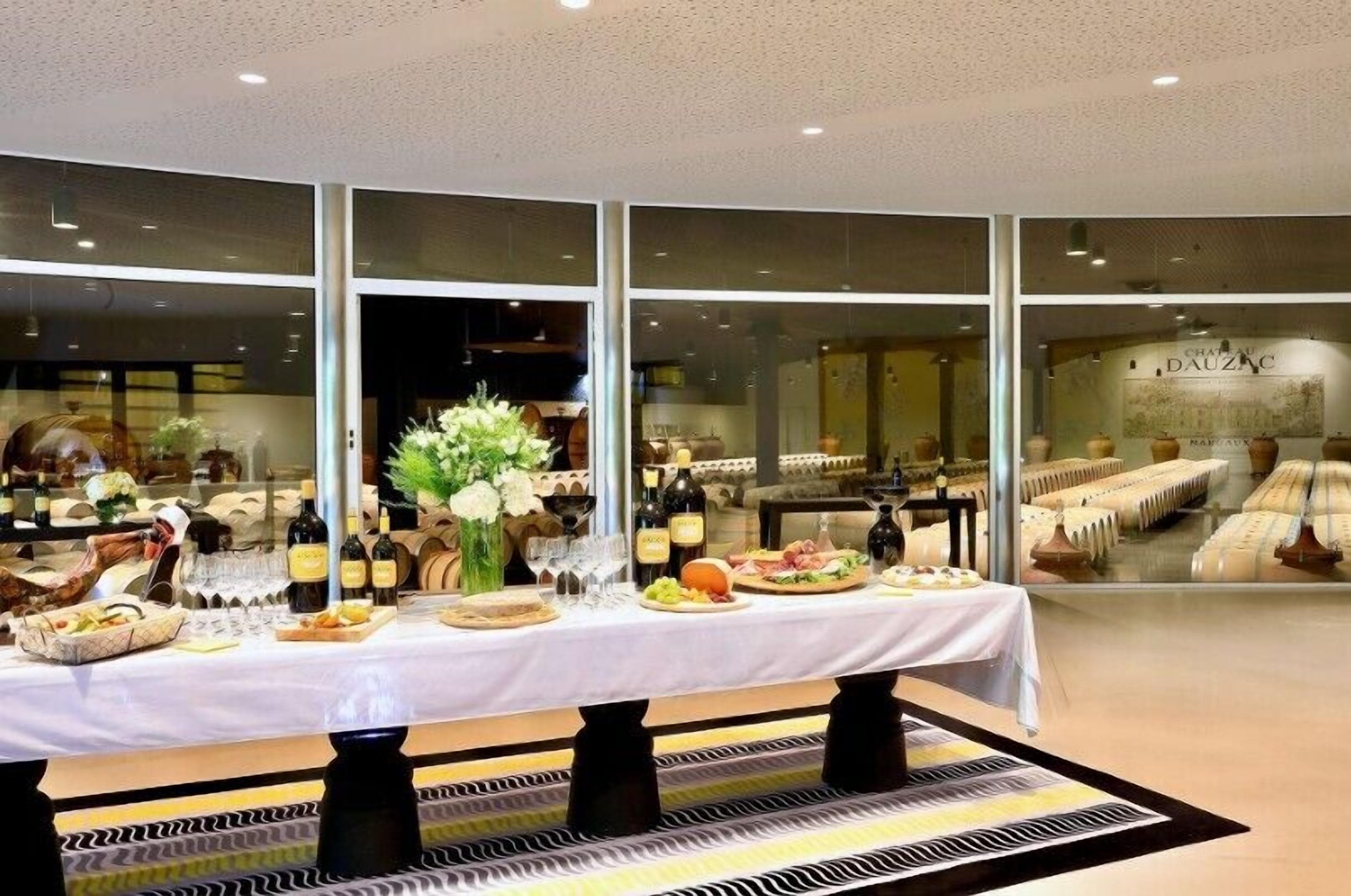 A dining area with a long table set for a meal, large windows, and a view of the interior.