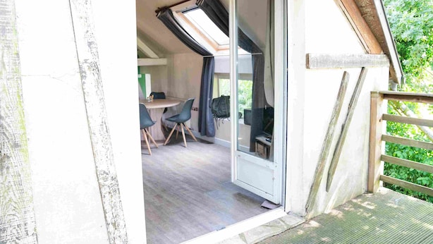 Une pièce dotée d’une porte-fenêtre coulissante donnant sur un balcon, d’une petite table avec des chaises et d’une fenêtre avec des rideaux.