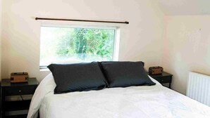 Une chambre à coucher avec un grand lit, une fenêtre, une table de chevet et un luminaire suspendu.