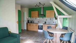 Une cuisine de taille réduite avec des meubles en bois, une table à manger avec des chaises et un canapé vert.
