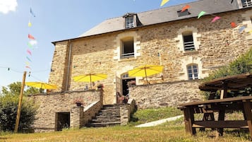 Experience the charm of this traditional building, featuring a symmetrical facade with evenly spaced windows and a central entrance, complemented by a welcoming outdoor area with seating.