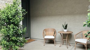 Eine Terrasse mit zwei Korbstühlen, einem kleinen Tisch und einem Blumentopf.