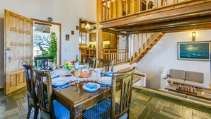 Ein Essbereich mit einem Holztisch, gedeckt für sechs Personen, umgeben von Stühlen. Eine Treppe führt zu einer oberen Ebene mit einem Balkon.