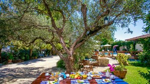 Ein Essbereich im Freien mit einem Picknicktisch, gedeckt für ein Frühstück, umgeben von üppiger Vegetation und einem Pool im Hintergrund.