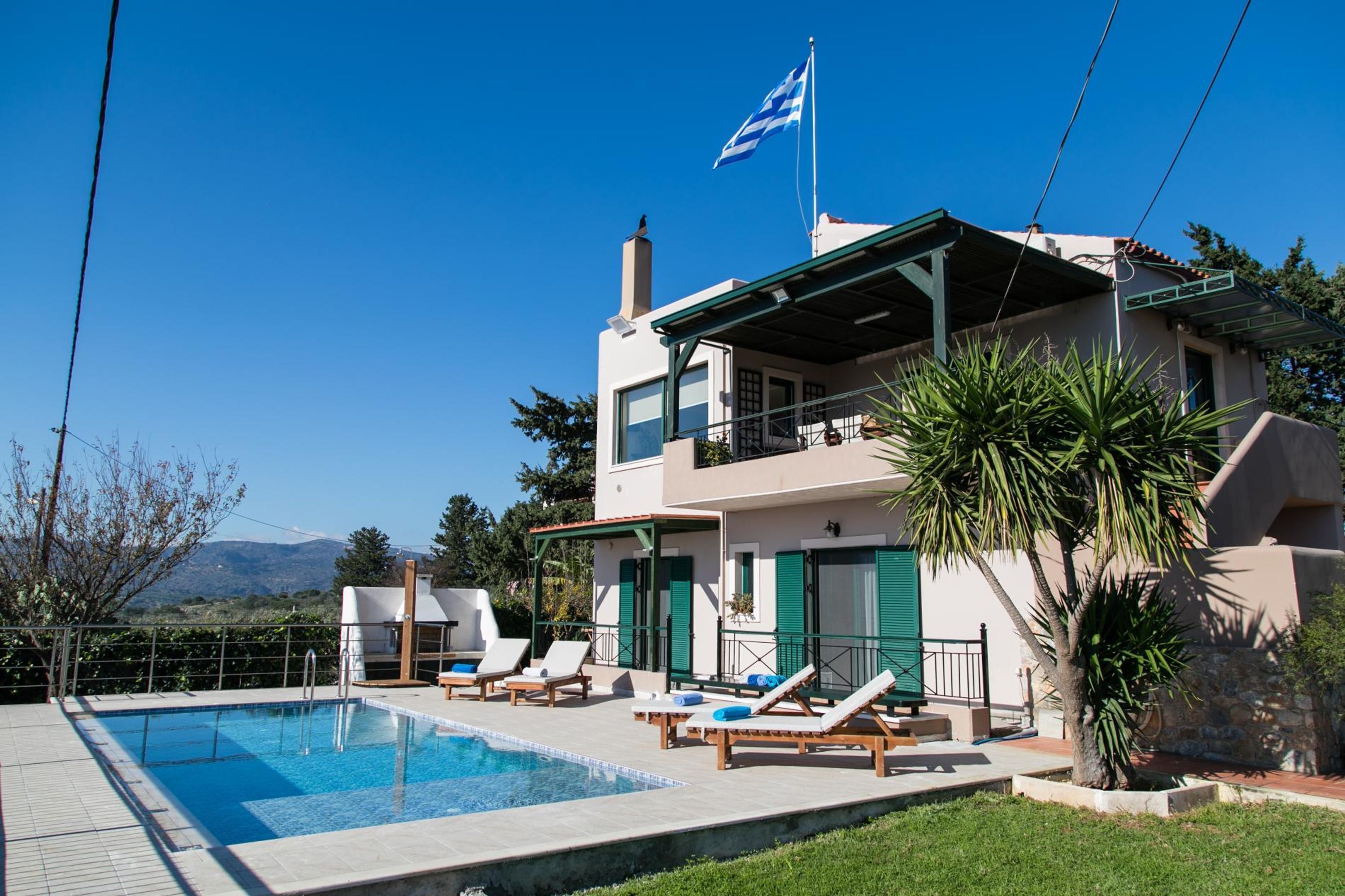 A two-story building with a swimming pool, lounge chairs, and a flag.
