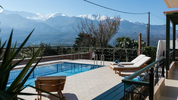 Un espace piscine offrant une vue sur des montagnes enneigées, une terrasse en bois et un fauteuil de relaxation.