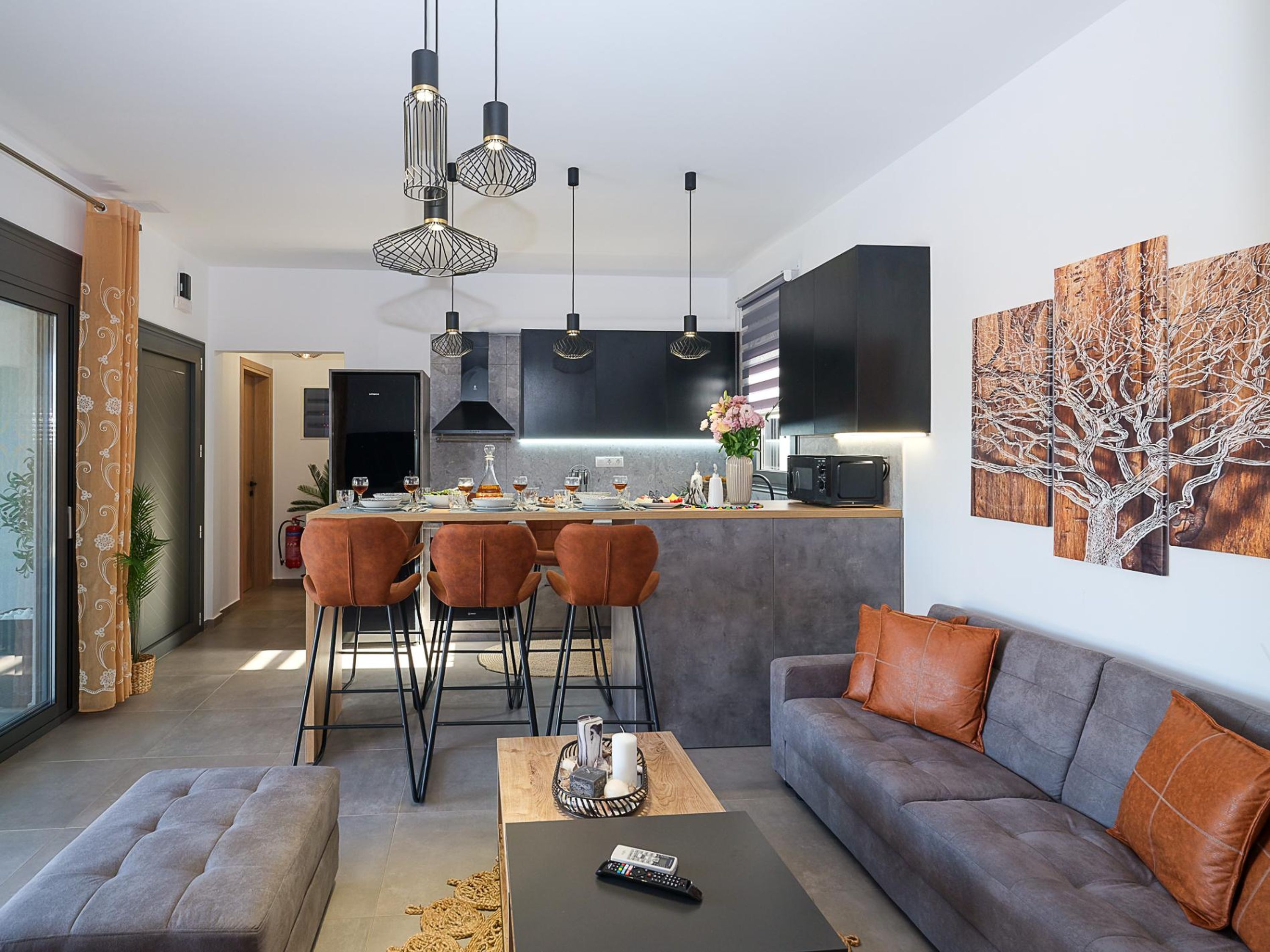 Een moderne woonkamer met een grijze bank, een salontafel, en een eethoek met een keuken op de achtergrond.
