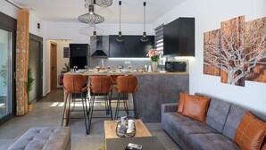 A modern living room with a grey sofa, a coffee table, and a dining area with a kitchen in the background. - Villa Eleonas With Private Swimming Pool (Rethymno)