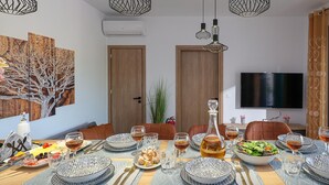 A dining area with a wooden table set for a meal, surrounded by chairs, and overhead lighting. - Villa Eleonas With Private Swimming Pool (Rethymno)