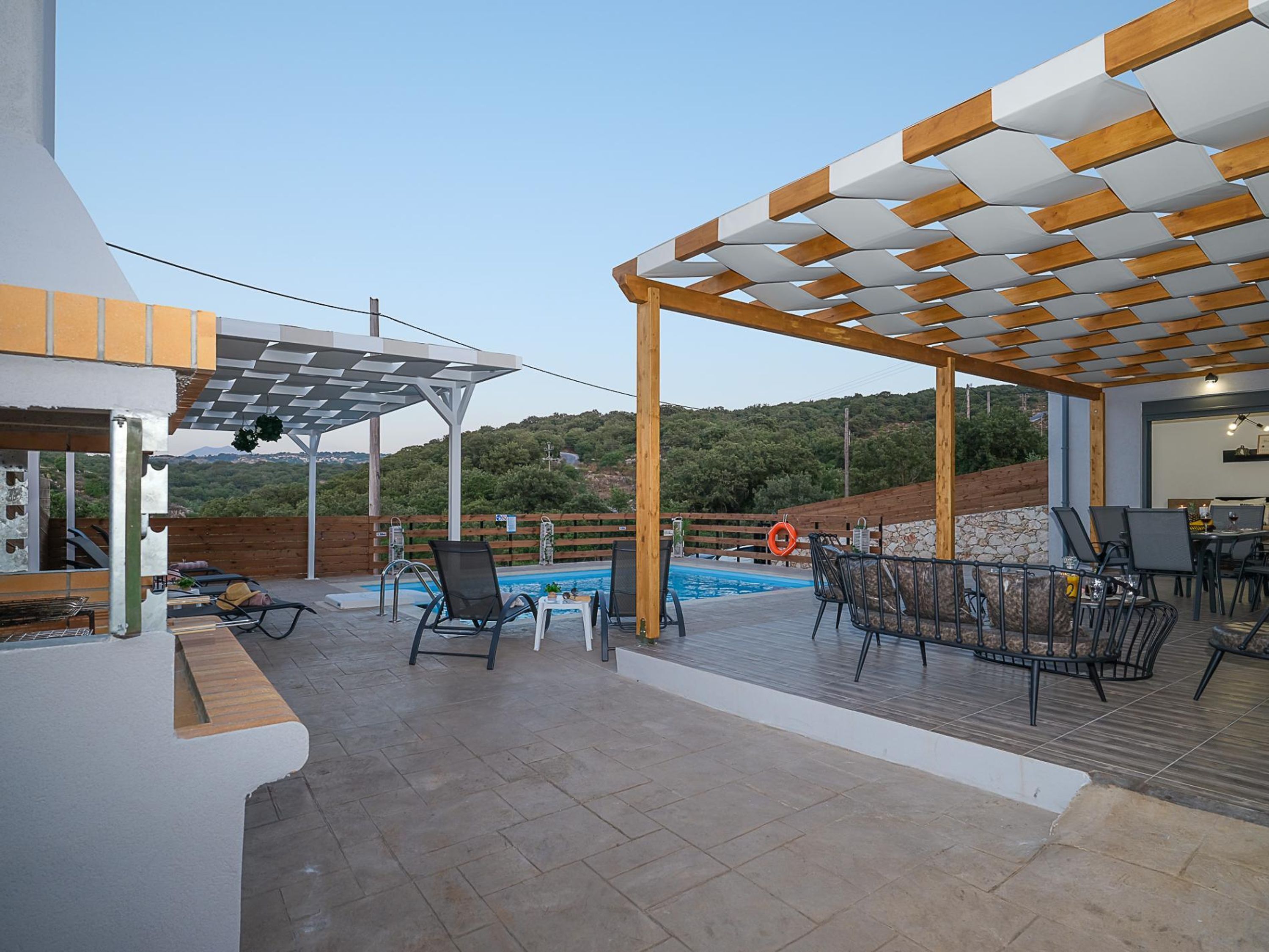 Un patio exterior con piscina, mobiliario y una pérgola.