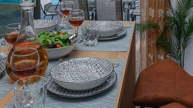 Un coin repas avec une table dressée pour deux personnes, une bouteille de vin et un saladier rempli de salade.