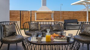 An outdoor patio with a barbecue grill, seating area with chairs and cushions, and a table set with food and drinks. - Villa Eleonas With Private Swimming Pool (Rethymno)
