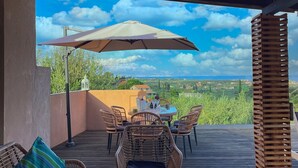 An outdoor patio with wicker furniture, a table with a bowl of fruit, and a view of the landscape. - Villa De La Vita Alykes (Zakynthos)