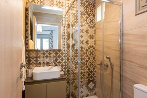 A bathroom with a glass-enclosed shower, a sink with toiletries, and patterned tiles.