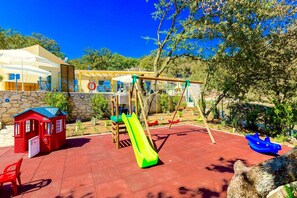 Un parque infantil con tobogán, columpios y una casita roja.
