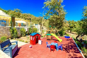 A children's play area with a slide, swings, and a small red playhouse.
