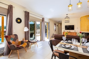 A modern living room with a dining area, large windows, and a flat-screen TV. - Villa Trules With Private Swimming Pool (Rethymno)