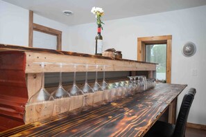 A wooden bar counter with wine glasses and a bottle of wine. - Meadow Rue Retreat • Aurora Views Near Fairbanks (North Pole, AK)