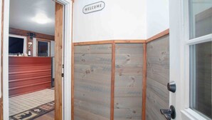 A hallway with a wooden panel wall, a welcome sign, and a door with a handle. - Meadow Rue Retreat • Aurora Views Near Fairbanks (North Pole, AK)
