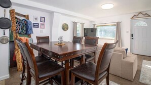 Een eetgedeelte met een houten tafel en stoelen, een televisie en een bank in een goed verlichte kamer met uitzicht op het omliggende landschap.
