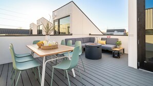 Una terraza moderna al aire libre con una mesa de madera, sillas verdes, un sofá gris y un reposapiés negro.