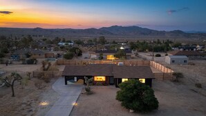 A single-story house with a covered patio, surrounded by desert landscape and mountains in the background. - Good Vibes Only by AvantStay | Modern Chic | Grill, Fire Pit + Hammocks (Joshua Tree)
