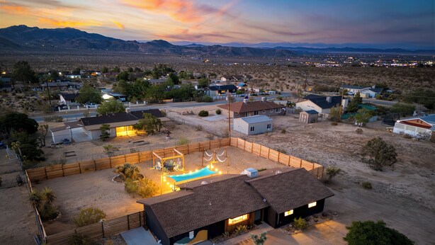A residential area with a house featuring a swimming pool, surrounded by a fenced yard and desert landscape. - Good Vibes Only by AvantStay | Modern Chic | Grill, Fire Pit + Hammocks (Joshua Tree)