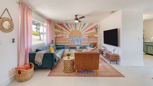 A living room with a sofa, a coffee table, a rug, and a wall with a sun design and the name "Joshua Tree". - Good Vibes Only by AvantStay | Modern Chic | Grill, Fire Pit + Hammocks (Joshua Tree)
