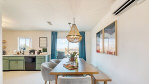 A modern kitchen with green cabinets, a dining area with a wooden table and chairs, and a large window with blue curtains. - Good Vibes Only by AvantStay | Modern Chic | Grill, Fire Pit + Hammocks (Joshua Tree)