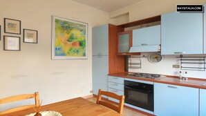 A compact kitchen with light blue cabinets, a wooden dining table, and a colorful abstract painting on the wall. - De Angeli District Apartment 2 (Milano)